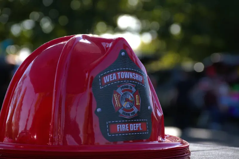 Red plastic junior firefighter helmets with the Wea Township shield, stacked at a community event.